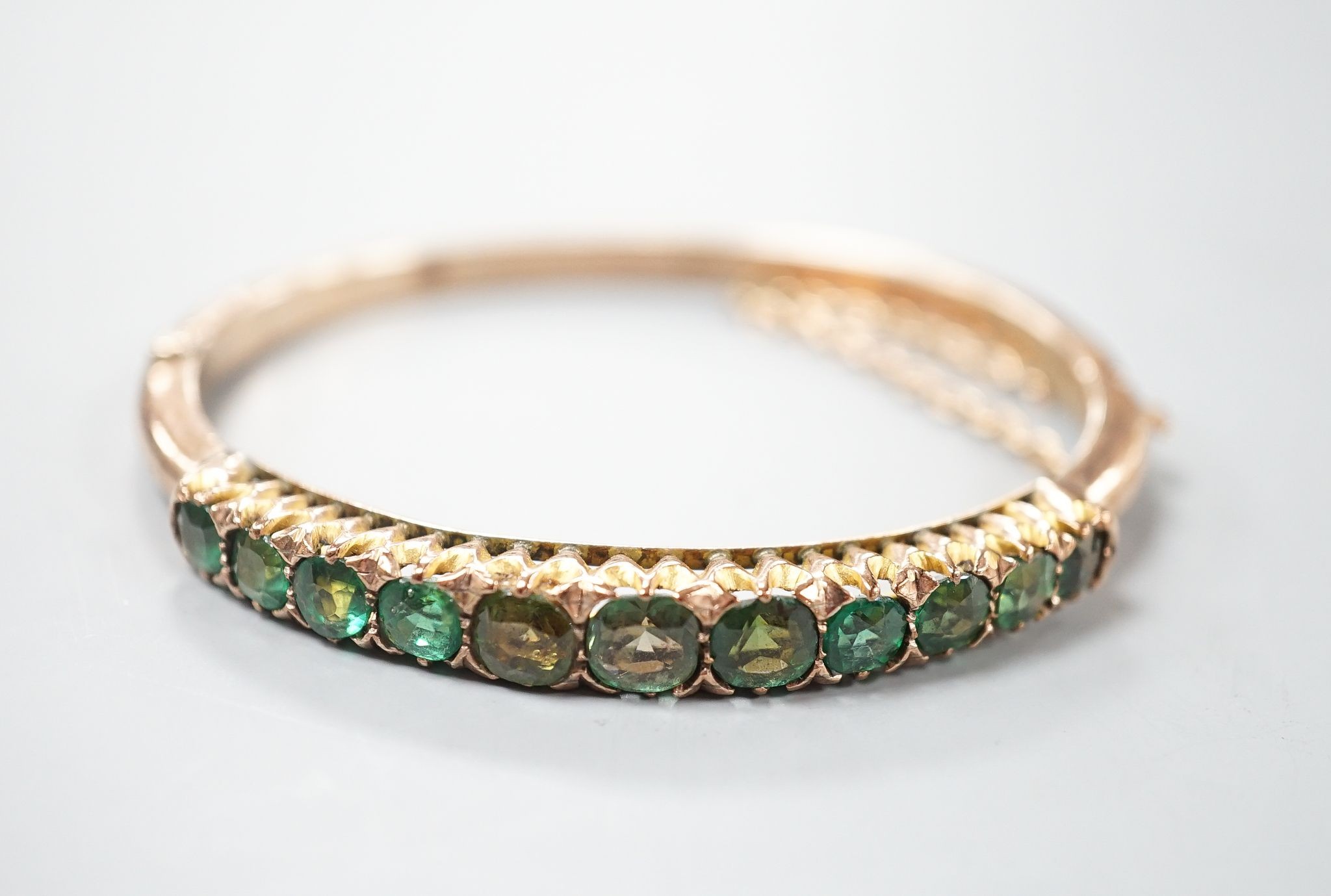 An Edwardian 9ct and graduated eleven green stone doublet set hinged bracelet, interior diameter 56mm, gross 12.6 grams.